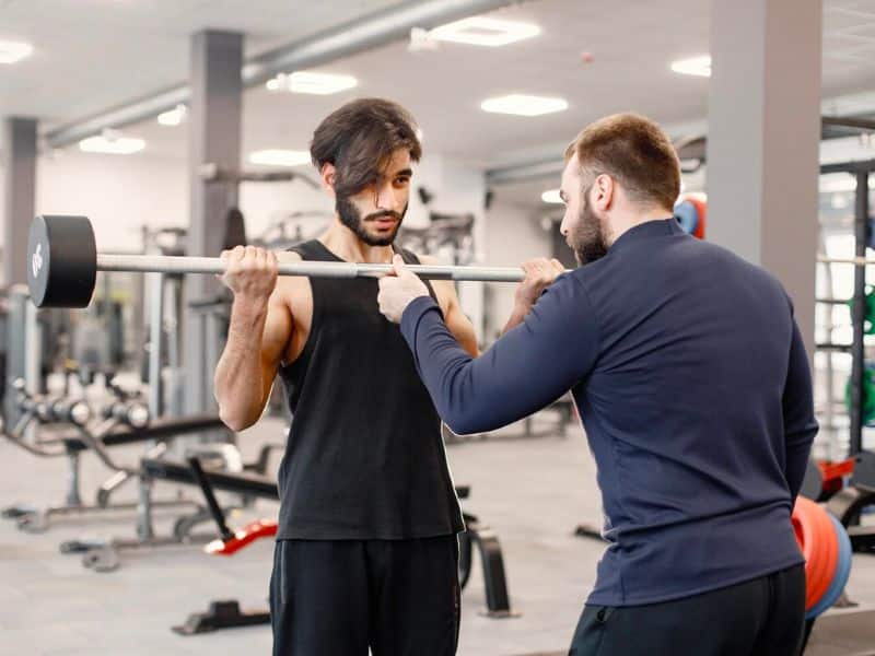man doing biceps curl with trainer 