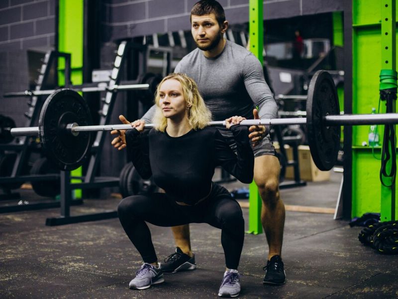 a lady doing squat with his trainer 