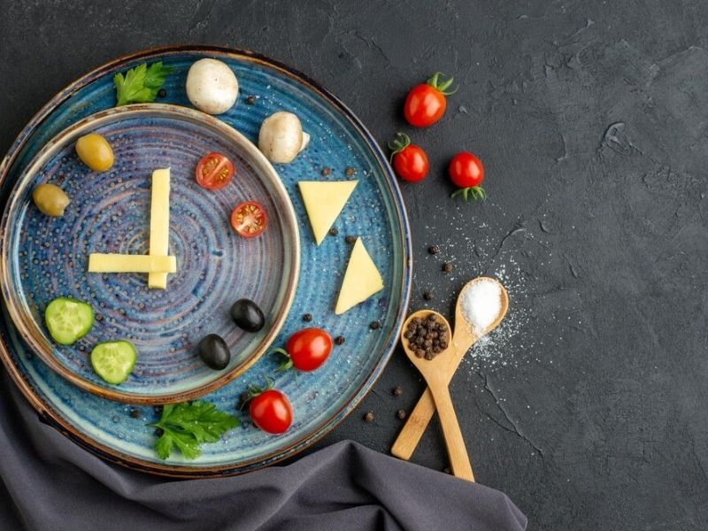 A clock with healthy snacks placed at different times around it.
