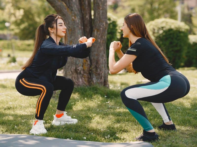 two ladies doing squats in a park
