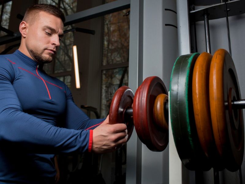 An image of a person confidently adding more weight to a dumbbell.
