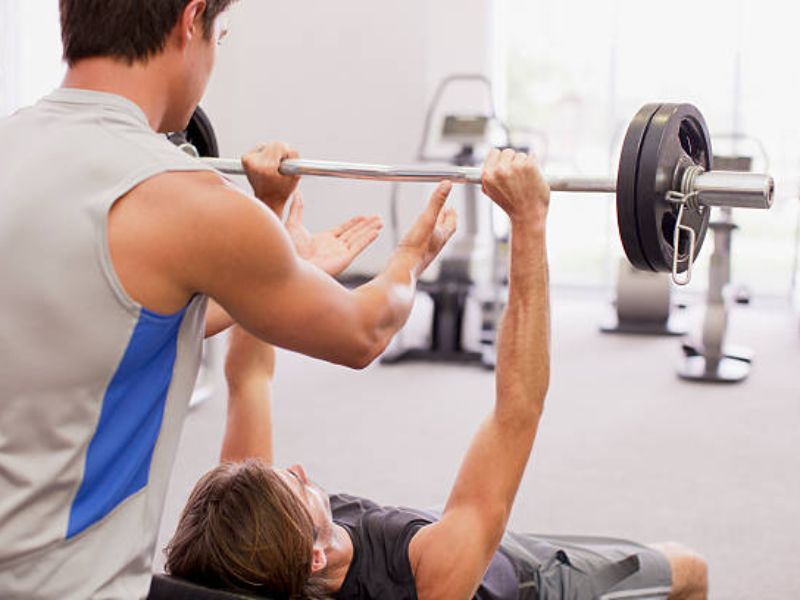 a person lifting weights with spotter